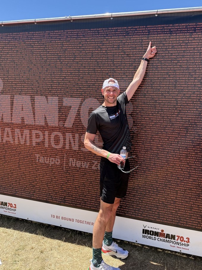 Joachim Becker zeigt auf seinen Namen an der Namenswand der IRONMAN 70.3 Weltmeisterschaft in Taupō, Neuseeland